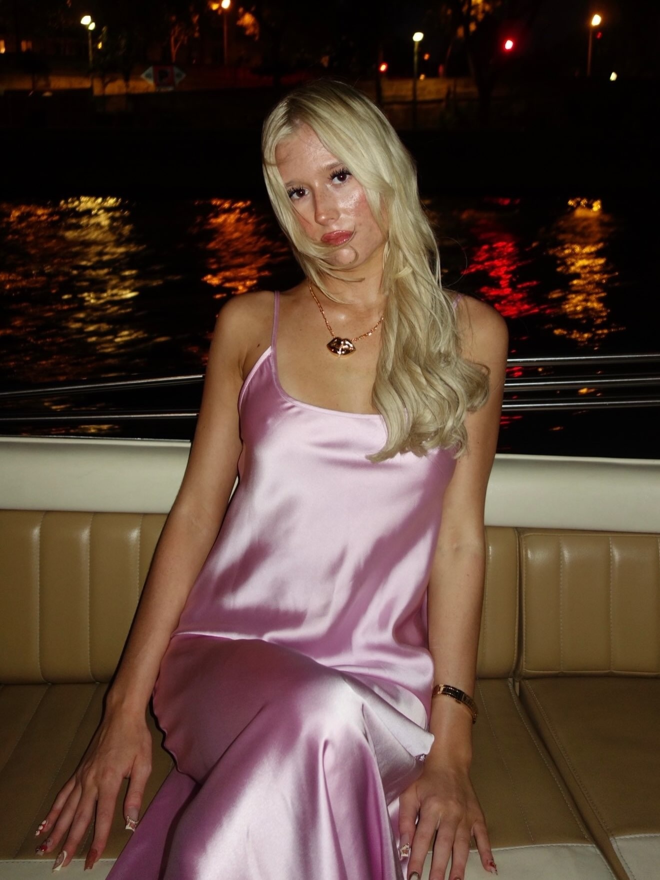 Samara in a pink satin dress beside the water at night